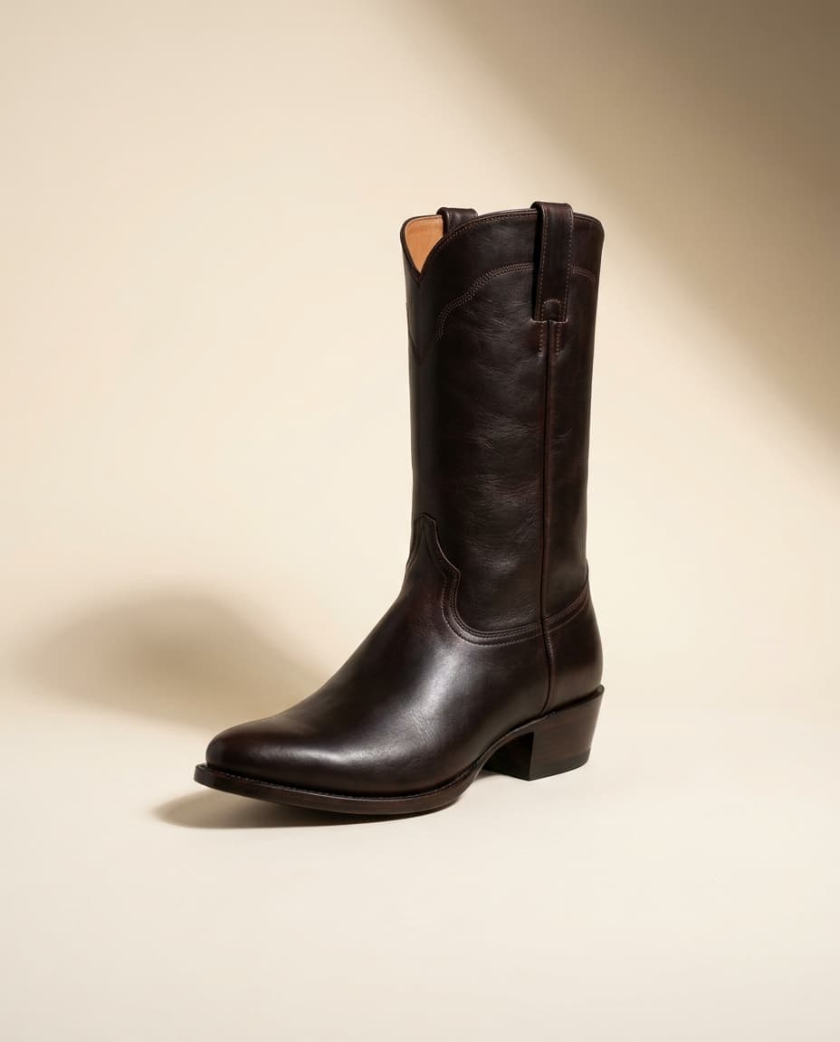Editorial product photograph of The Arroyo, a dark whiskey full-grain leather snip-toe stovepipe western boot with a 12 inch shaft and an underslung leather heel