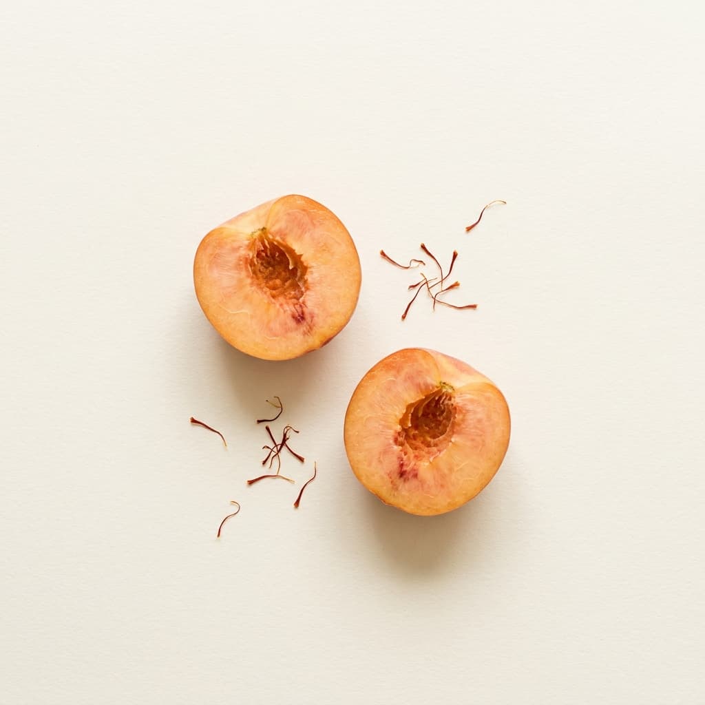 A can of Peach Saffron Bloom soda nestled with ripe peach halves and saffron threads on cream paper.
