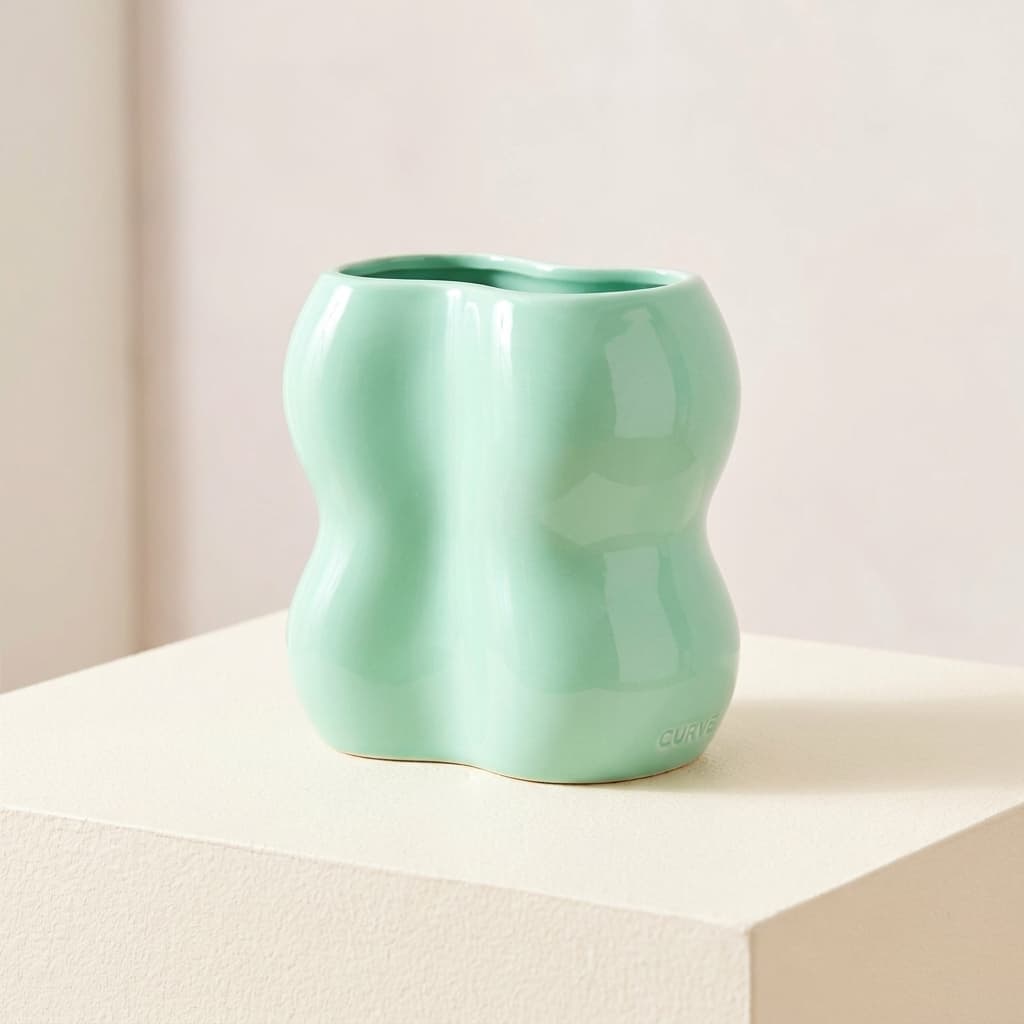 Curve Wave Vase, a wavy ceramic vase in mint, photographed on a cream surface.