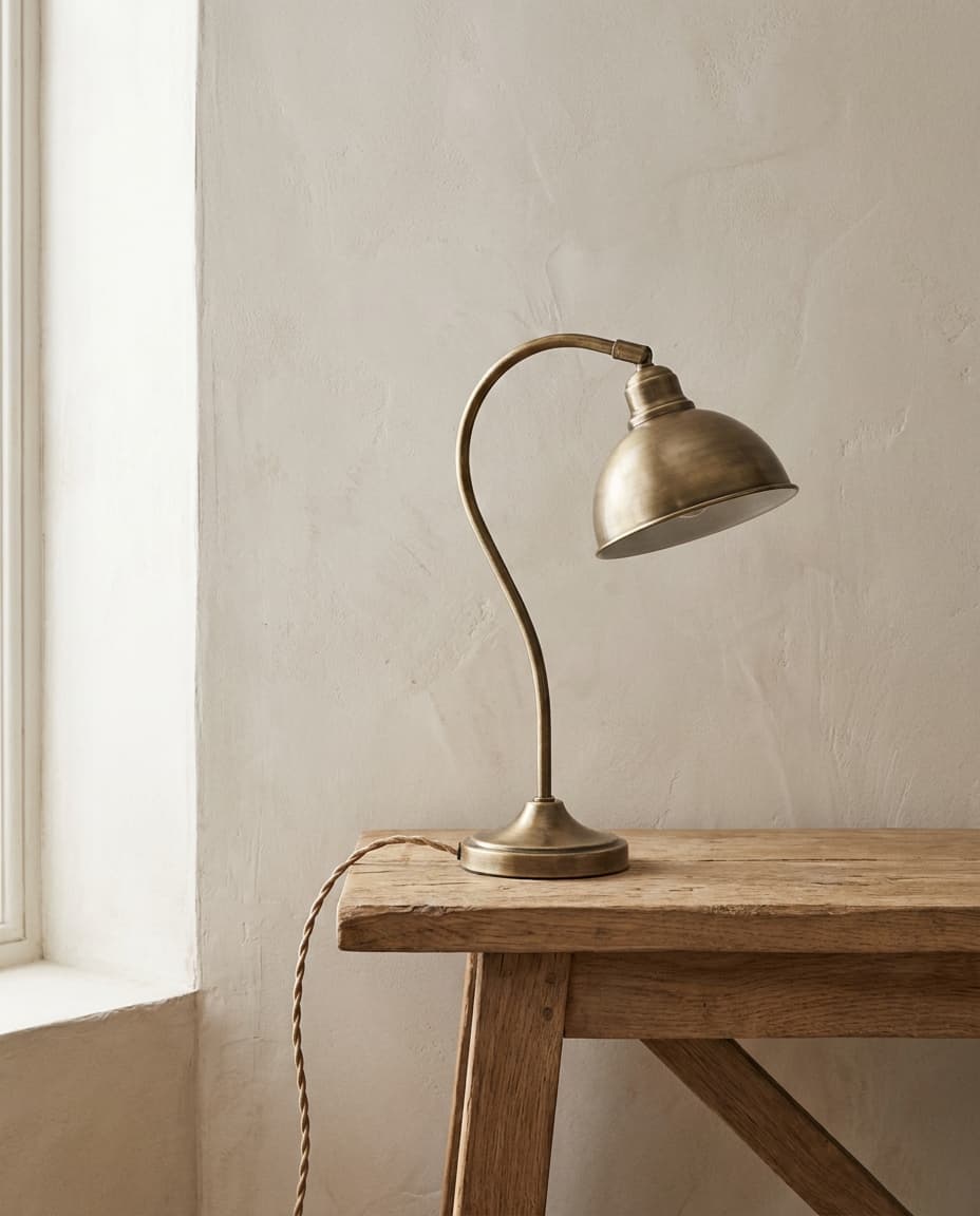 A single brushed brass pendant lamp hanging against a soft plaster wall, casting a warm pool of light.
